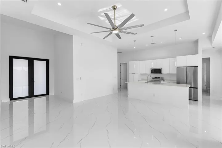 Kitchen featuring open floor plan, a tray ceiling, white cabinets, appliances with stainless steel finishes, and pendant lighting