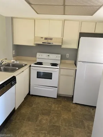 Kitchen with white appliances, light countertops, under cabinet range hood, and cream cabinets