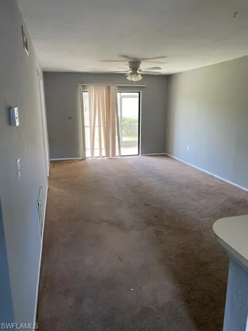 Carpeted empty room with ceiling fan and baseboards