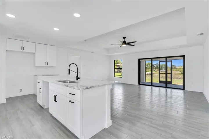 **Previous Model Photo** Kitchen featuring an island with sink, white cabinetry, ceiling fan, and a raised ceiling