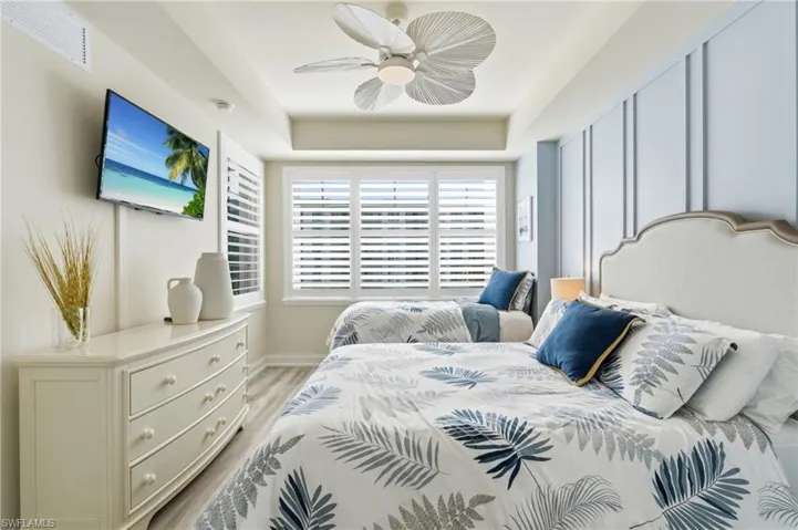 Room featuring two beds, a mounted television, and plantation shutters