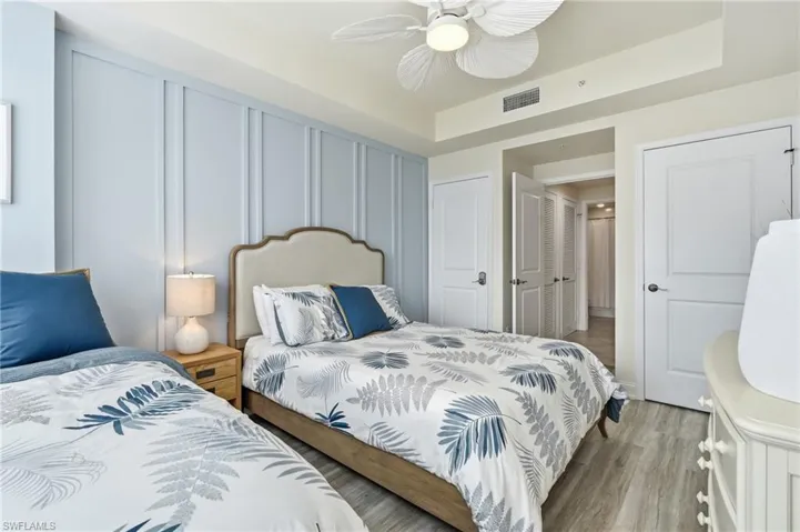 Bedroom featuring a light blue accent wall with vertical paneling, light wood-finish flooring, and a ceiling fan with integrated lighting