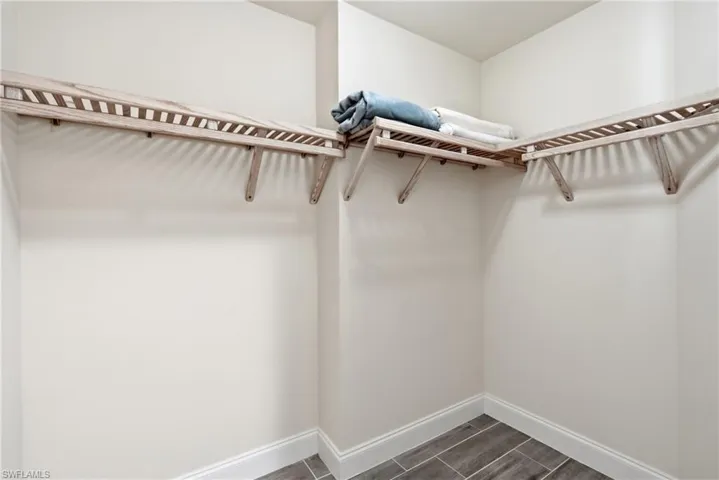 Walk-in closet with L-shaped wood shelving, light neutral wall paint, white baseboards, and wood-finish tile flooring