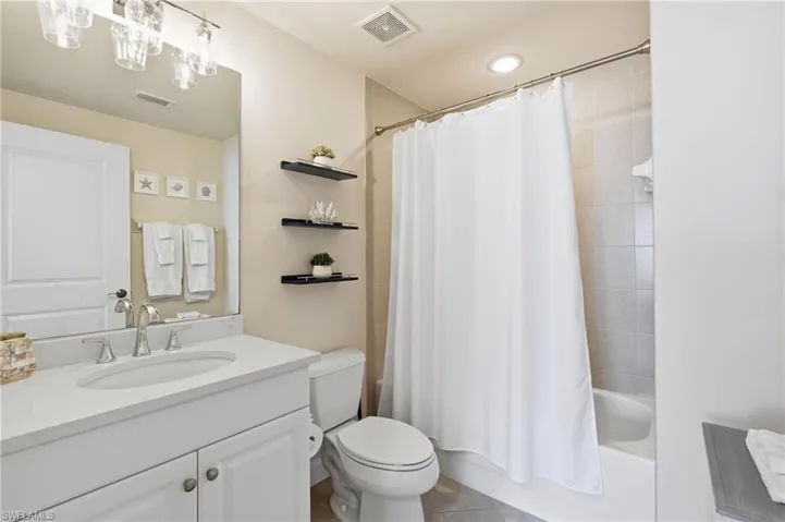 Bathroom featuring a white vanity with an undermount sink, a large wall mirror, and a combination tub and shower with tiled surround
