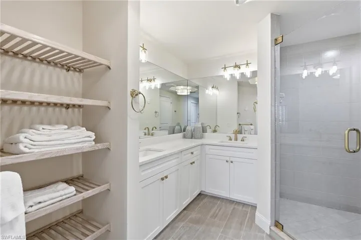 Contemporary bathroom featuring a spacious glass-enclosed shower with large format tile, dual vanity with white cabinetry and integrated sinks, and ample built-in shelving