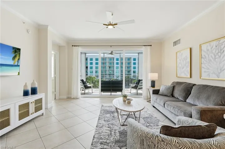 Living area featuring light-colored tile flooring, crown molding, and a ceiling fan