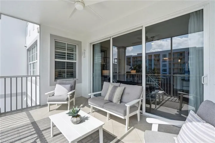 Covered balcony featuring a ceiling fan, sliding glass doors, a window with horizontal blinds, and a metal railing