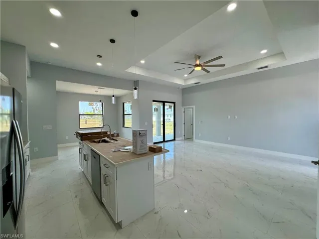 Kitchen featuring a tray ceiling, light marble finish flooring, appliances with stainless steel finishes, pendant lighting, and a center island with sink