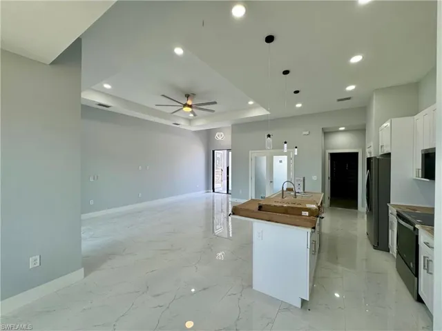 Kitchen with white cabinetry, a tray ceiling, stainless steel appliances, decorative light fixtures, and a center island with sink