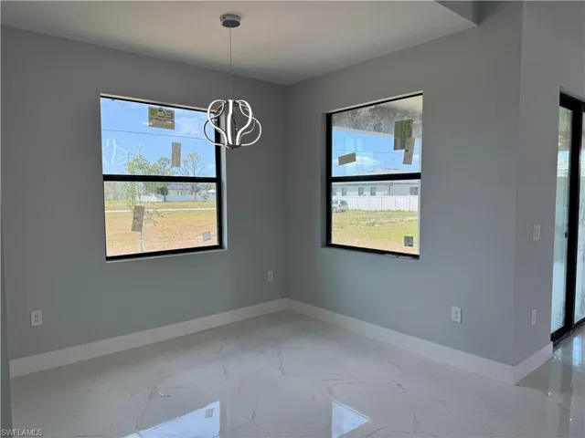 Unfurnished dining area featuring light marble finish floors, plenty of natural light, and a chandelier