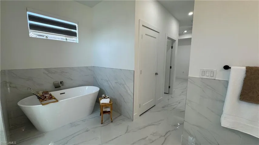 Full bathroom with a soaking tub, marble tiled floors, tile walls, wainscoting, and recessed lighting