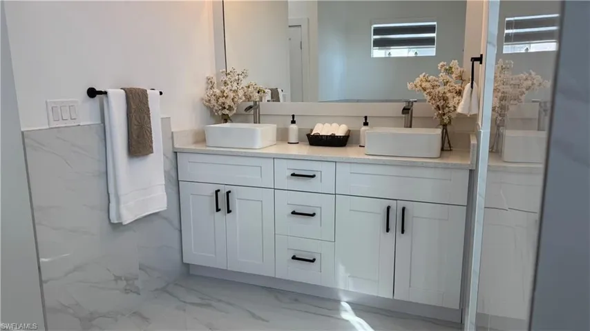 Bathroom with light marble finish floors, double vanity, and a walk in shower