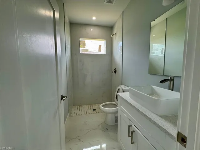 Bathroom featuring a shower stall, vanity, light marble finish flooring, and recessed lighting
