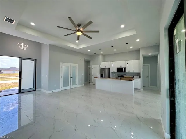 Unfurnished living room with a raised ceiling, light marble finish flooring, and recessed lighting