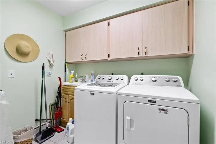 Clothes washing area with sink, light tile patterned flooring, independent washer and dryer, and cabinets