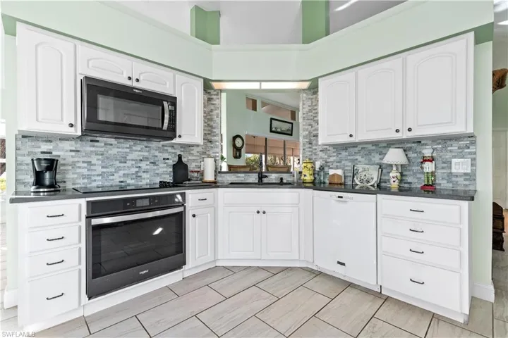 Kitchen featuring white cabinets, backsplash, black appliances, a high ceiling, and sink