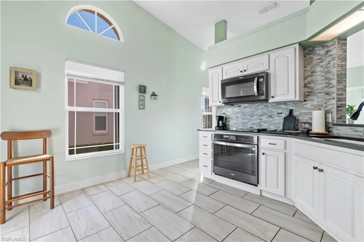 Kitchen featuring backsplash, appliances with stainless steel finishes, white cabinetry, high vaulted ceiling, and sink