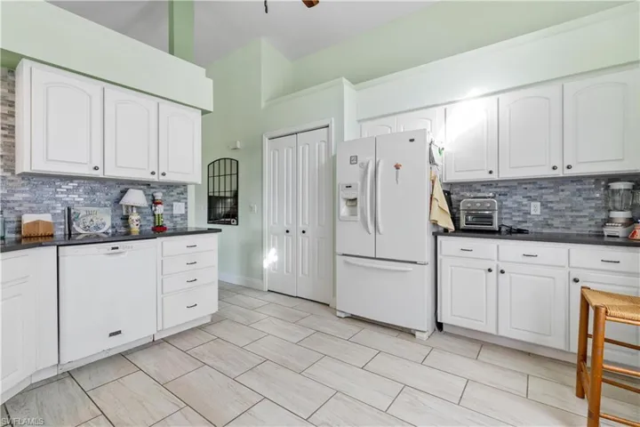 Kitchen with white appliances, white cabinetry, and decorative backsplash