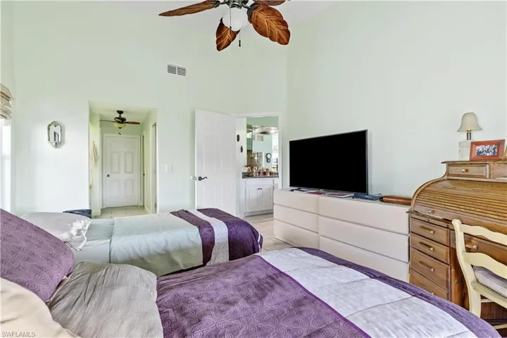 Tiled bedroom featuring ensuite bath, a high ceiling, and ceiling fan