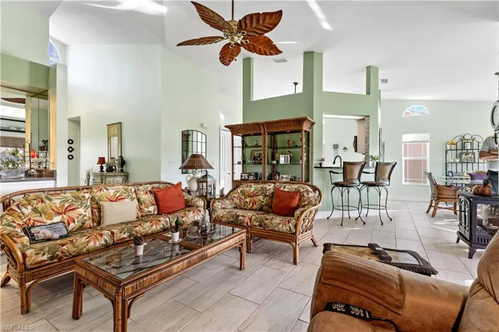 Living room featuring ceiling fan, high vaulted ceiling, a wood stove, and plenty of natural light