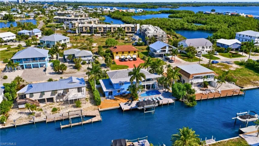 Waterfront property featuring a private boat dock, backyard swimming pool, and multiple palm trees - Virtually Edited Image