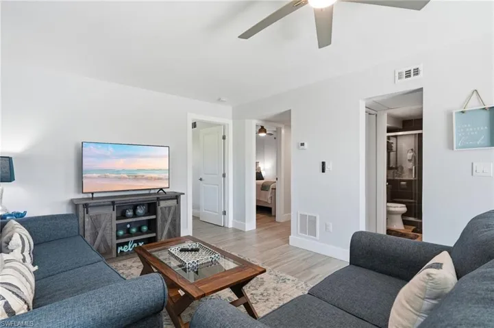 Open-concept living area featuring light wood-finish flooring, a contemporary ceiling fan, and crisp white walls - Virtually Edited Image