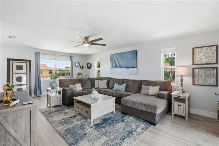 Spacious living area featuring light wood-finish flooring, recessed lighting, and a contemporary ceiling fan - Virtually Edited Image