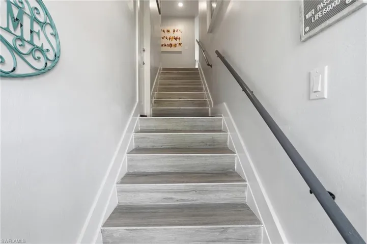 Staircase featuring wood-finish treads, a contrasting white riser, and a dark metal handrail - Virtually Edited Image
