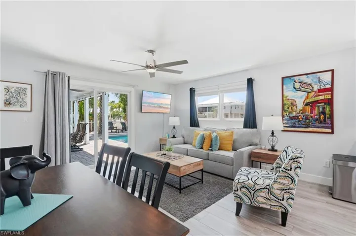Open-concept living space featuring wood-finish flooring, a contemporary ceiling fan, and sliding glass doors opening to an exterior patio with a swimming pool - Virtually Edited Image