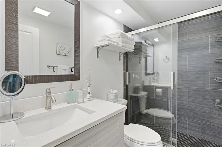 Bathroom featuring a frameless glass shower enclosure with gray horizontally tiled walls and a dark mosaic tile floor - Virtually Edited Image