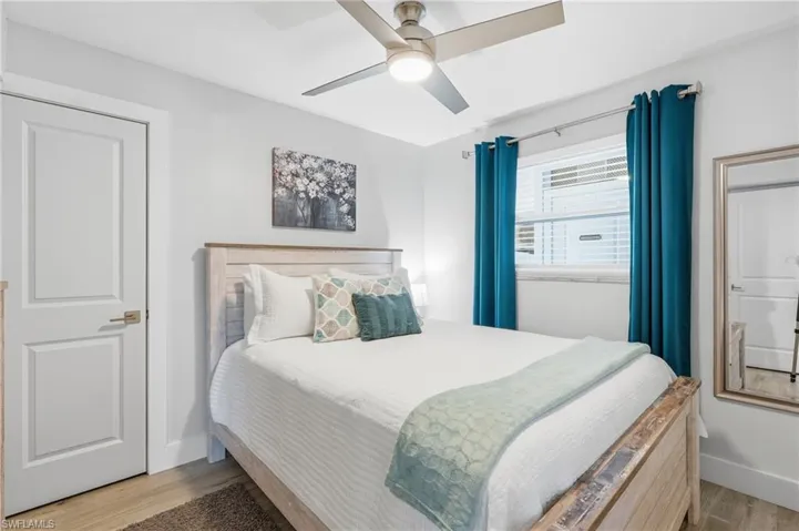 Bedroom featuring light wood-finish flooring, a contemporary ceiling fan, and a paneled interior door - Virtually Edited Image