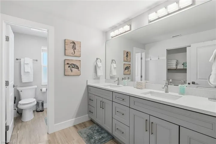 Dual vanity with gray shaker cabinetry, integrated sinks, and light-toned countertops - Virtually Edited Image