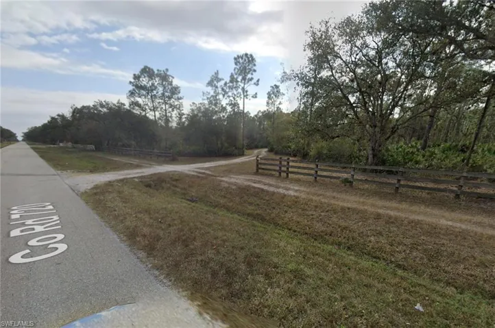 Paved road frontage with a gravel access road, bordered by a rustic wooden fence