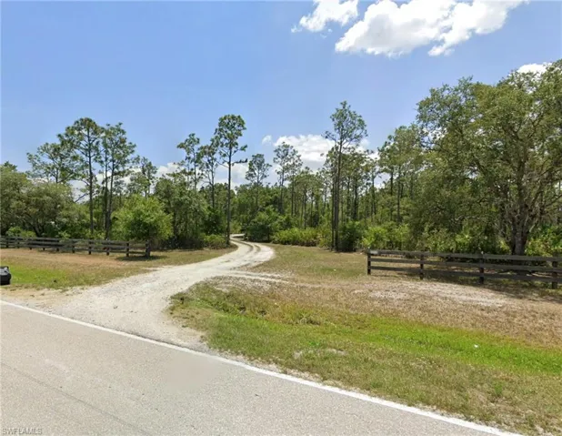 Gravel driveway extending into a wooded landscape, bordered by a split-rail fence
