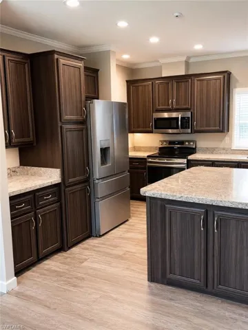 Kitchen featuring wood-finish cabinetry, light-toned countertops, stainless steel appliances, recessed lighting, and wood-look flooring