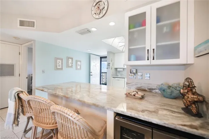 Kitchen with light stone countertops, white cabinetry, recessed lighting, a peninsula, and a kitchen bar