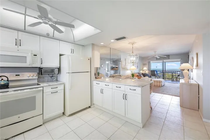 Kitchen featuring ceiling fan, white appliances, open floor plan, and white cabinetry