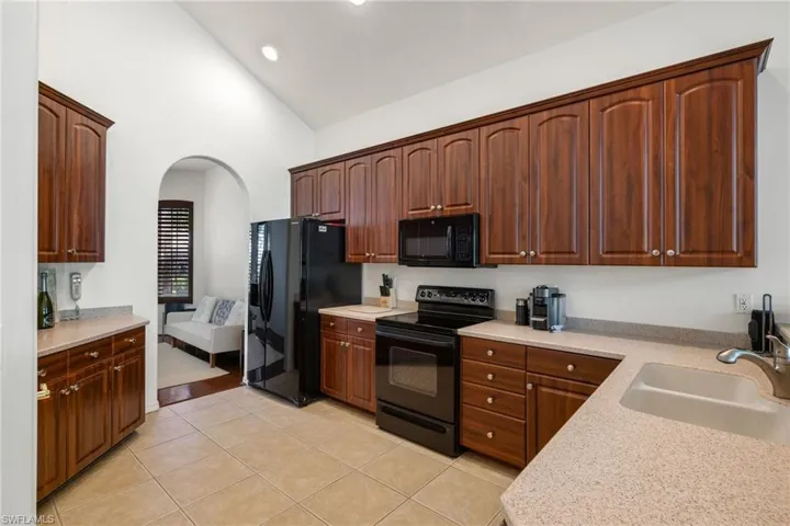 Kitchen with light tile patterned floors, arched walkways, a sink, light countertops, and black appliances