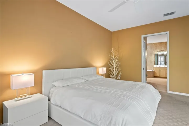 Bedroom featuring visible vents, baseboards, ceiling fan, ensuite bath, and light colored carpet