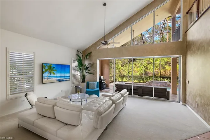 Carpeted living room featuring high vaulted ceiling, baseboards, and a ceiling fan