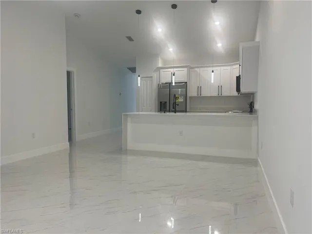 Kitchen featuring stainless steel fridge with ice dispenser, light marble finish floors, a peninsula, white cabinetry, and light countertops
