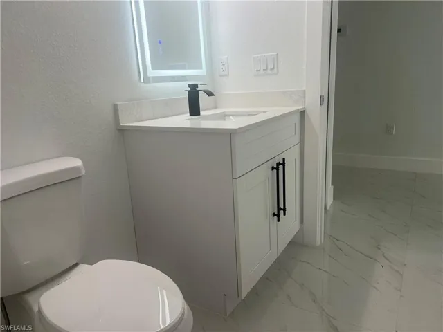 Bathroom with marble finish flooring, vanity, and a textured wall