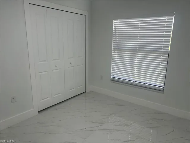 Unfurnished bedroom featuring light marble finish floors and a closet