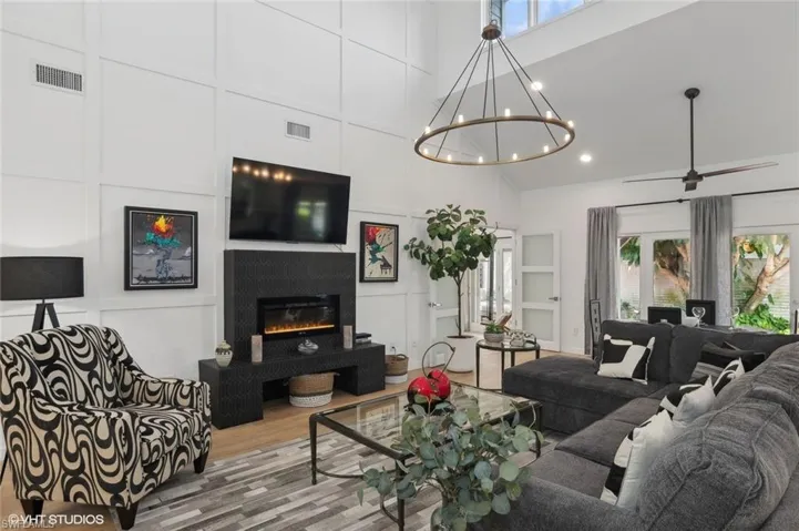 Living room featuring hardwood / wood-style floors, a high ceiling, a tile fireplace, and ceiling fan with notable chandelier