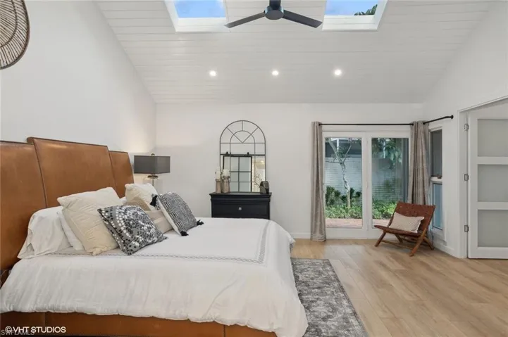 Bedroom with high vaulted ceiling, ceiling fan, light wood-type flooring, and a skylight