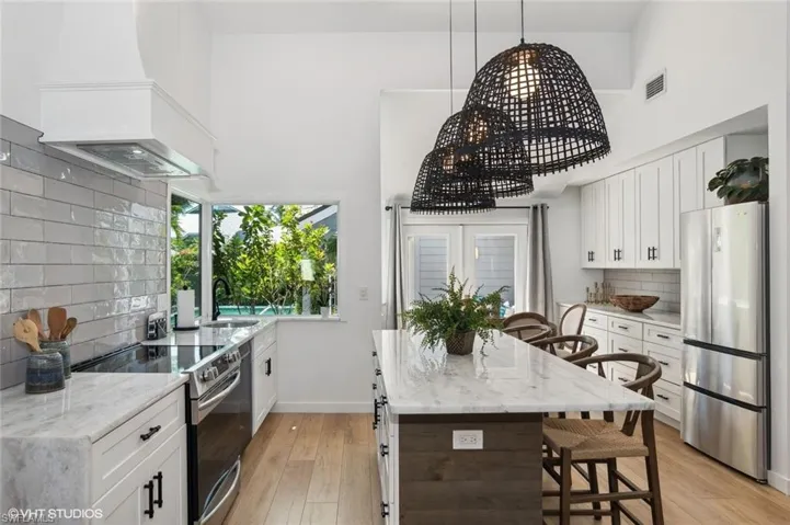 Kitchen featuring light hardwood / wood-style floors, stainless steel appliances, backsplash, custom exhaust hood, and a center island