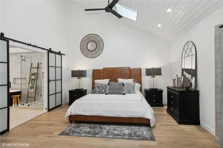 Bedroom with a barn door, light hardwood / wood-style floors, high vaulted ceiling, and a skylight