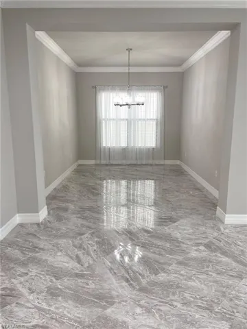 Unfurnished dining area featuring crown molding, light marble finish flooring, and a chandelier