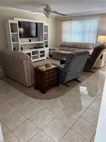 Living area featuring a ceiling fan, light tile patterned floors, and crown molding