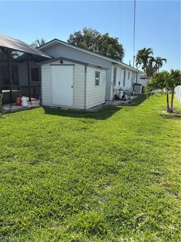 Rear view of house featuring a lawn, an outbuilding, and a storage unit